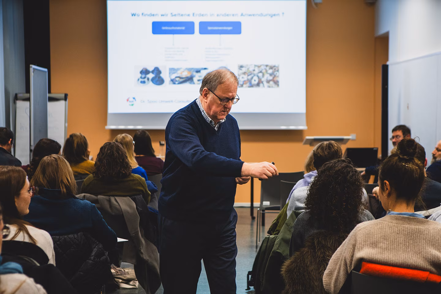 Helmut Spoo verteilt kleine Magnete an Zuhörer in einem gut gefüllten Hörsaal der VHS.