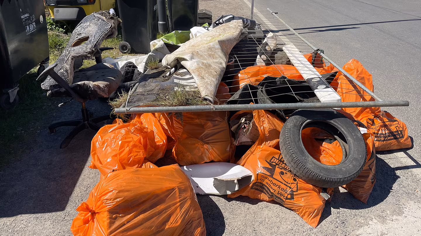 Ergebnis 3/3 beim Cleanup in Lövenich Ein großer Berg aus orangen Müllsäcken. Oben drauf liegt ein Kapputer Bauzaun, ein Bürostuhl und ein Autoreifen.