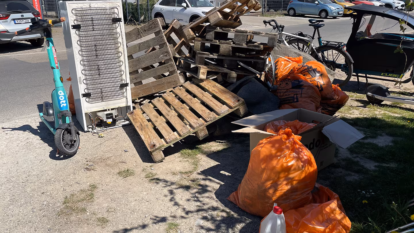 Ergebnis 2/3 beim Cleanup in Lövenich Ein großer Berg aus orangen Müllsäcken. Im Hintergrund ein Kühlschrank und ein Berg aus Paletten.