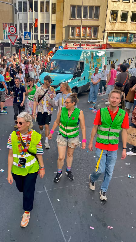 Glas_CSD_20260705_Fußweg_450x800 Das Team ist fertig mit sammeln und geht vor dem Wagen beim CSD her