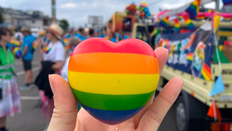 Ein Regenbogenherz im Vordergrund, im Hintergrund der Pritschenwagen und das Team verschwommen
