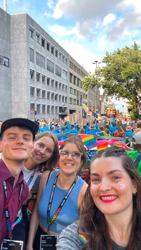 Glas_CSD_20260705_WagenParty_450x800 Das Team feiert auf dem Pritschenwagen den Abschluss, im Hintergrund weitere Gruppen in der CSD Parade