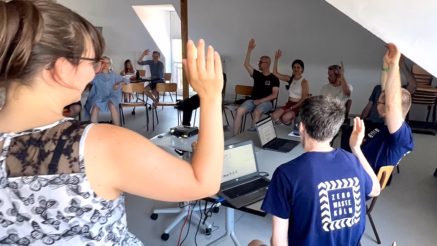 Abstimmung bei Mitgliederversammlung Mitglieder von Zero Waste Köln sitzen im Halbkreis und heben die Hand zur Abstimmung.