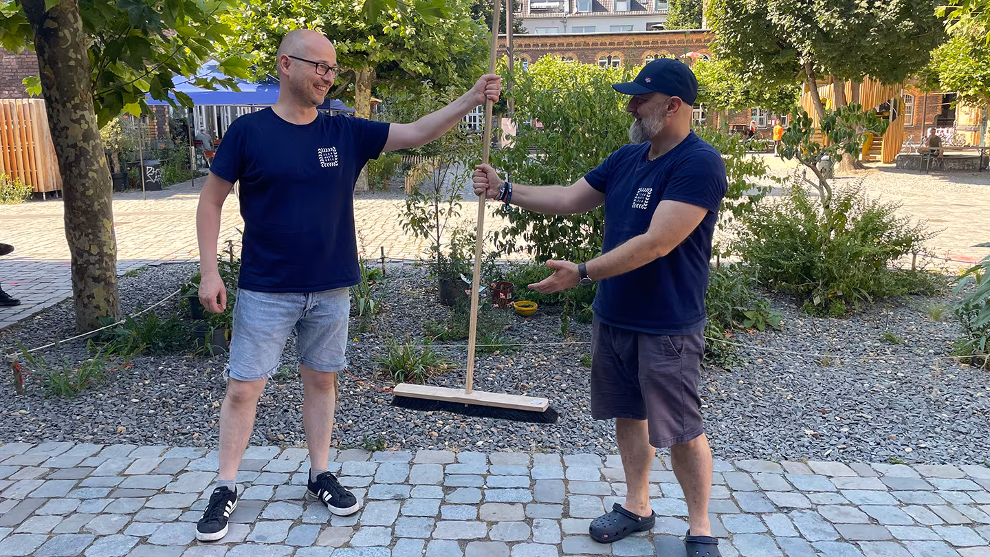 Michael ergibt symbolisch einen Holzbesen an Franz