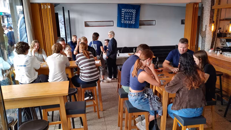 Das GLORIA Café ist gefüllt mit Spielegruppen, im Hintergrund hängt ein Banner mit dem Logo von Zero Waste Köln