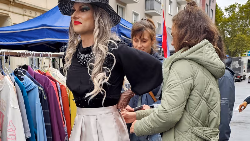Laufaktion auf dem Tag des guten Lebens 2026 Tricia Trash zieht ihren neuen Rock an, die Besucherin schließt den Verschluss hinten am Rücken